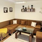Ein Wohnzimmer mit braunem Sofa, Glas-Tisch und Wandregal mit Büchern.