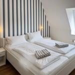 Two single beds with white linens and towels. Striped wall decor. Skylight.