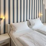 Two beds with white linens, striped wall, and nightstands with wall lamps.