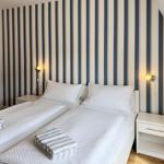 Two beds with white bedding and striped towels against a striped wall.