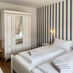 Two beds with white linens and striped towels. Striped wall and mirrored wardrobe.