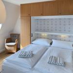 Two beds with white linens and towels. Wooden furniture and window.