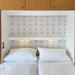 Two beds with white pillows and bedding under a wall panel with sailboat motif.