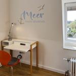 Desk with chair and wall decoration Meer macht glücklich. Window with view of residential area.