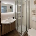 Bathroom with shower, sink and toilet. Tiled wall and wooden floor.