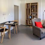 Dining area with table and chairs, armchair with pillow, bookshelf, and wall art.