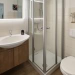 Bathroom with shower, sink, and toilet. Wooden cabinet and mirror with lighting.