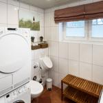 Badezimmer mit Waschmaschine, Trockner, WC und Holzbank.