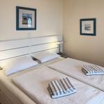 Zimmer mit Doppelbett, weißen Bettwäsche und zwei Handtüchern. An den Wänden hängen Bilder.