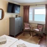 Zimmer mit Bett, Fernseher, Schrank und zwei Stühlen vor Fenster.