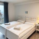 Zwei Einzelbetten mit weißen Laken und Handtüchern. Fensterblick auf Außengelände.