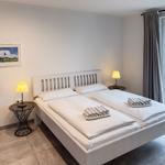 Schlafzimmer mit Doppelbett, zwei Nachttischen und Fensterblick auf Garten.