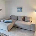 Ein Wohnzimmer mit grauem Ecksofa, zwei Bildern an der Wand und einer Stehlampe.