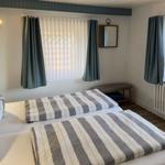 Zimmer mit zwei Betten, Fenstern mit Vorhängen und Spiegel an der Wand.
