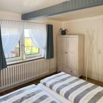 Zwei Betten mit gestreiften Bettwäsche, Fenster mit Vorhängen und Kleiderständer.