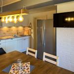 Küche mit Essbereich, Kühlschrank, TV und Holztisch mit Stühlen.