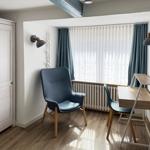 Ein Raum mit Schreibtisch, Stuhl und Kleiderschrank neben großem Fenster.