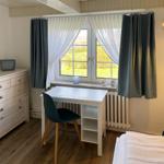 Schlafzimmer mit Schreibtisch, Bett und Fenster mit Blick auf Grünflächen.