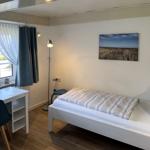 Ein Schlafzimmer mit Bett, Schreibtisch und Fenster. Wandbild und Stehlampe.