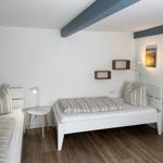 Zimmer mit zwei Betten, Holzboden und Wandregalen. Deckenbalken und Wandbild sichtbar.