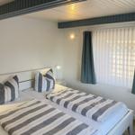 Zwei Betten mit gestreiften Bettwäsche, Fenster mit Vorhängen und Nachttisch mit Lampe.