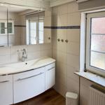 Badezimmer mit Waschbecken, Spiegelschrank und Fenster mit getöntem Glas.