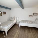 Zwei weiße Betten mit Streifenbetten, Holzboden und blaue Balken an der Decke.