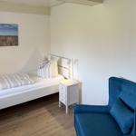 Ein Schlafzimmer mit Bett, Nachttisch und blauem Sessel. Wandbild zeigt eine Landschaft.