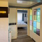 Schlafzimmer mit Bett und Fenster. Flur mit TV und bunten Glasscheiben.