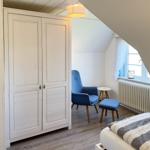 Schlafzimmer mit weißem Schrank, blauer Sitzgelegenheit und Fenster mit Vorhang.