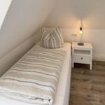 Schlafzimmer mit Einzelbett, Nachttisch und Stehlampe unter schrägen Dachdecken.