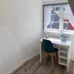 Ein Arbeitszimmer mit Schreibtisch, Stuhl und Fenster mit weißen Vorhängen.