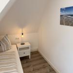 Schlafzimmer mit Dachschräge, Bett, Nachttisch und Strandbild an der Wand.