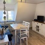 Essbereich mit Tisch, Stühlen, Sofa und Fernseher. Holzboden und Fenster mit Vorhängen.
