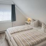 Room with two beds, window with curtains, and bedside table with lamp.