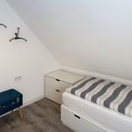 Bedroom with sloped ceiling, bed, nightstand, and blue stool.