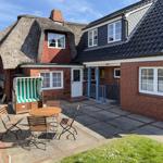 House with thatched roof, terrace with garden furniture and green lawn.