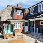 House with thatched roof, terrace, and beach chair. Entrance with blue pillars.