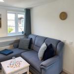 Living room with gray sofa, table, and wall clock. Window with curtains and wall picture.