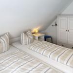 Two beds with striped bedding, nightstand with lamp, and white wardrobe.
