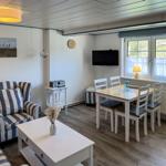 Wohn- und Essbereich mit Sofa, Tisch und Fernseher. Fenster mit Vorhängen.