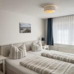 Zimmer mit Doppelbett, zwei Nachttischen und Fenster mit Vorhängen.