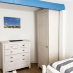Schlafzimmer mit weißem Schrank, Schrank und Bett mit Streifenbezug.