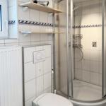Badezimmer mit Dusche, Toilette und Fenster. Fliesen mit Wellenmuster.
