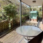 Terrace with table, chairs, and beach chair. Wooden deck, stone wall, and plants in the background.