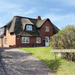 Red house with thatched roof and white windows. A sign with the house name stands in front.