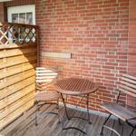 Terrasse mit Holztisch und zwei Stühlen vor roter Ziegelwand