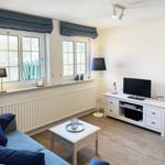 Wohnzimmer mit Sofa, Fernseher und zwei Fenstern mit blauen Vorhängen.