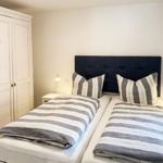 Zwei Betten mit Streifenbetten und dunklem Kopfteil, weiße Nachttische und Schrank.