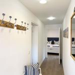 Flur mit Garderobe, Spiegel und Blick in Schlafzimmer mit Bett und Kissen.